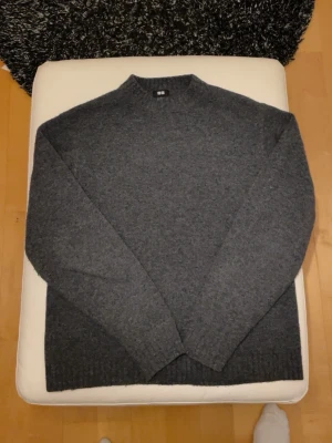 Mörkgrå stickad tröja från Uniqlo - Mysig mörkgrå stickad tröja från Uniqlo i storlek S. Tröjan har en enkel, klassisk design med ribbade muddar vid hals, ärmslut och nederkant. Perfekt för kyliga dagar och passar till det mesta i garderoben.