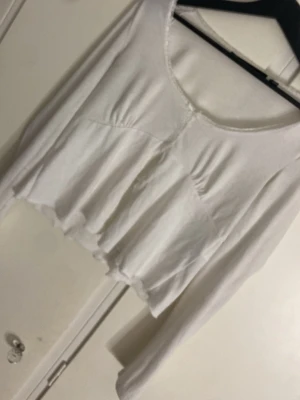 Vit blus med volang från Vero Moda - Säljer en vit blus från Vero Moda i storlek S. Toppen har lång ärm, rund halsringning och en volangdetalj nedtill som ger en söt och flowy look. Materialet känns mjukt och lätt, perfekt för vår och sommar. Passformen är normal och toppen är enkel att matcha.