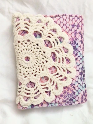 Handgjord anteckningsbok med virkat omslag - Unik anteckningsbok med mjukt, färgglatt tyg och virkat spetsmönster på omslaget. Perfekt för dig som vill skriva, rita eller samla tankar på ett personligt sätt. Passar både till skolan och som kreativ dagbok. A6 storlek ca 100 sidor