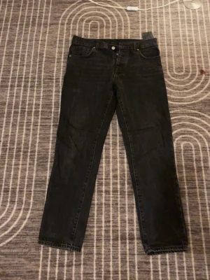 Svarta jeans från Zara, storlek 38 - Svarta jeans från Zara i klassisk femficksmodell. Jeansen har rak passform och normal midja, tillverkade i ett slitstarkt bomullsmaterial. Snyggt minimalistisk look med svarta sömmar och knappstängning framtill. Perfekt för dig som gillar stilrena och enkla jeans.