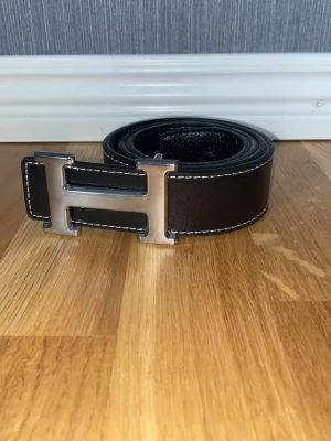 Svart bälte - Bilderna visar ett svart skärp med silverfärgat H-spänne och vit söm, inte en väst. Kan ej ge västbeskrivning.