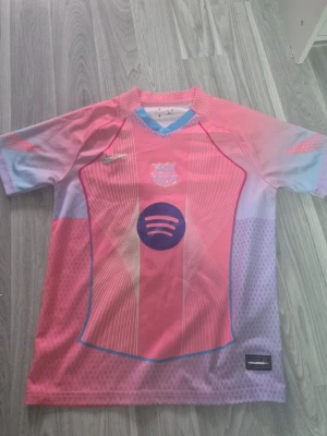 Rosa Lamine yamal xoncept tröja. - Bilderna visar en fotbollströja från FC Barcelona med Lamine Yamal och nummer 19, i rosa och lila toner med Spotify-logga. Spotify loggan är väldigt skrynklig och kan gå av. Den passar mig som är 150cm