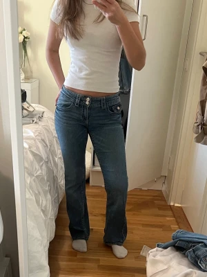 Blå bootcut jeans låg midja - Säljer ett par blå jeans med låg midja och bootcut-snitt. Jeansen har klassiska fem fickor, dubbla knappar i midjan och är tillverkade i jeansmaterial. Perfekta för dig som gillar en avslappnad och snygg stil.