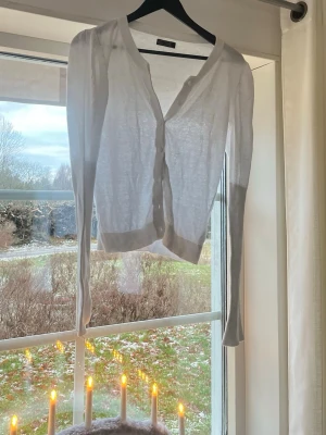 Vit tunn kofta med knappar - Säljer en supertunn och lätt vit kofta med långa ärmar. Koftan har ribbade kanter och stängs med matchande vita knappar framtill. Superfin och unik kofta! Storlek L men passar mer S och möjligtvis M 