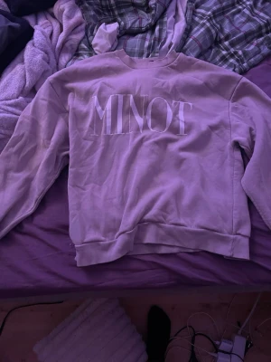 Ljuslila sweatshirt från Minot - Säljer en ljuslila sweatshirt från Minot med stor vit logotyp på bröstet. Tröjan har rund hals, ribbade muddar vid ärmslut och nederkant samt lång ärm. Perfekt för dig som gillar enkel och stilren design.