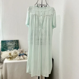 Vintage ljus mintgrön nylonklänning med spets - Söt ljus mintgrön nattlinne med plisserade detaljer och vit spets längs axlar och bröst. Är något genomskinlig. Enligt modellen har klänningen 3 knappar men det finns 2 extra hål om du vill fixa till fler knappar till den. Storlek: ONE SIZE. Dockan är i storlek 34.