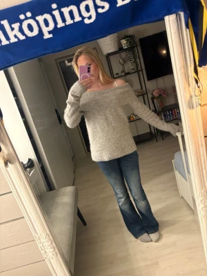 Grå offshoulder stickad tröja - Supermysig grå stickad tröja med offshoulder-design och bred ribbad kant upptill. Tröjan har lång ärm och en loose fit som gör den perfekt att slänga på sig när det är kyligt. Passar perfekt till jeans för en chill look.