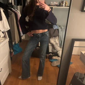 Blå bootcut jeans med låg midja - Säljer ett par klassiska blå jeans med bootcut och låg midja. Jeansen har fem fickor, snygga detaljer på bakfickorna med knappar och en rak, något utsvängd passform. Perfekta för dig som gillar en avslappnad men ändå trendig look. Jag är 169cm lång