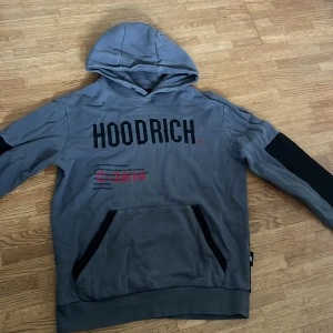 Grå hoodie från Hoodrich med tryck - Säljer en grå hoodie från Hoodrich i storlek medium. Tröjan har svart tryck framtill och coolt rött tryck med världskarta på ryggen. Huva, känguruficka och svarta detaljer på ärmar och ficka. Storlek M men passar även S