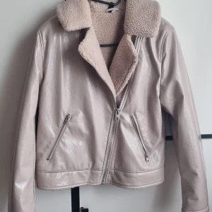 Beige teddyjacka med dragkedja, S - Säljer en beige teddyjacka med glansig yta och mjukt teddyfoder. Jackan har bred krage, två snedställda fickor med dragkedja och stängs med sned dragkedja framtill. Utsidan är i syntetmaterial och insidan i teddyfleece. Perfekt för kyliga dagar.