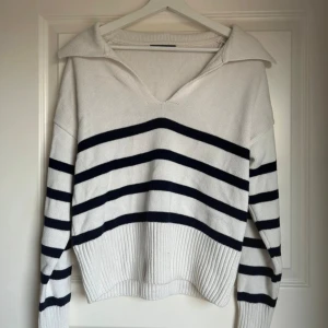 Randig stickad tröja från Gina Tricot - Skriv gärna innan! Superfin stickad tröja från Gina Tricot i vitt med mörkblåa ränder. Tröjan har en bred krage, v-ringning och långa ärmar.  Ganska kort