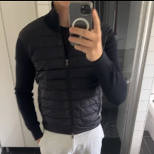 moncler cardigan - Snygg svart dunväst med quiltad design och hel dragkedja framtill. Västen har en stilren look och passar perfekt över en hoodie eller tröja. Den är lätt och smidig att bära, och ger extra värme utan att kännas klumpig.