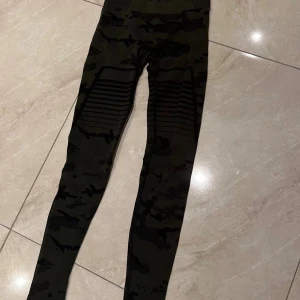 Gavelo sport wear leggings med ribbade detaljer - Snygga svarta och mörkgröna leggings med camouflage-mönster och ribbade partier över låren. Hög midja och tight passform, perfekta för träning eller chill. Stretchigt syntetmaterial som sitter skönt och följer kroppen.