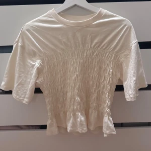 Ljusgul blus med volang från Gina Tricot - Säljer en ljusgul topp från Gina Tricot. Toppen har korta ärmar, smockad midja och en söt volang längst ner. Rund halsringning och en clean look som är lätt att styla med jeans eller kjol.