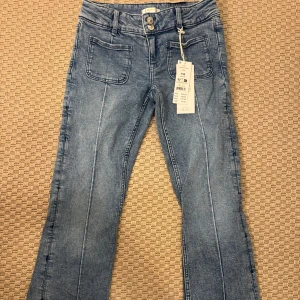 Blå bootcut jeans med fickor - Snygga ljusblå jeans från Gina Tricot med bootcut-modell och markerade sömmar längs benen. Jeansen har två framfickor och två bakfickor samt dubbla knappar i midjan. Perfekta för dig som gillar en trendig och avslappnad stil.