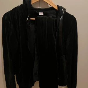 Svart  hoodie med huva samt byxor från Gina tricot  - Mjuk och  svart kofta med mjukis byxor . Tröjan har dragkedja framtill, huva med breda snören och långa ärmar. Perfekt för en chill och trendig look. Båda storlek s.