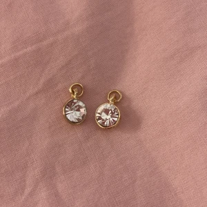 Guldiga berlocker med glittrande stenar 💎💎💎 - Säljer ett par runda berlocker med gnistrande klara stenar infattade i guldfärgad metall. Enkla men ändå riktigt snygga och perfekta för att ge lite extra bling till din look!!! ✨💎✨💎✨💎