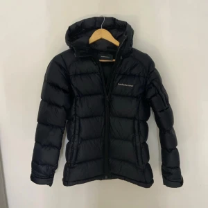 Svart dunjacka Peak Performance - Svart dunjacka från Peak Performance med huva och dragkedja framtill. Jackan har flera praktiska fickor, både invändigt och utvändigt. Perfekt för kalla dagar och har en stilren look. Använd en vinter och är helt utan defekter. Kostar ca 4000kr att köpa ny. Hör av dig om du har några frågor 💗