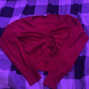 Röd croppad topp med snörning - Säljer en röd långärmad croppad topp från C med snygg snörning och rynkdetalj framtill. Toppen har v-ringad hals och är tillverkad i ett ribbat material som ger en cool och trendig look. Perfekt för dig som gillar att sticka ut med färg och detaljer.