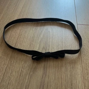 Svart smalt hårband  med rosett - Säljer ett svart smalt hårband med en söt rosett framtill. Hårbandet har en enkel och stilren design.  Materialet känns mjukt och flexibelt, troligtvis syntet. Perfekt accessoar för att ge outfiten en extra detalj.