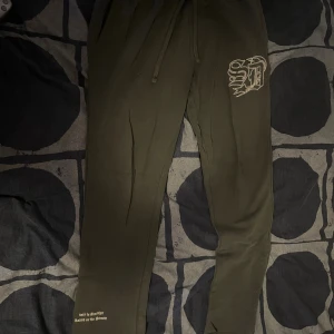 Mörkgröna mjukisbyxor med tryck - Snygga mörkgröna mjukisbyxor från Supply & Demand med snörning i midjan och coolt tryck på benet. Sköna att ha på sig och perfekta för chill dagar. Textdetaljer vid benslut ger extra stilpoäng.