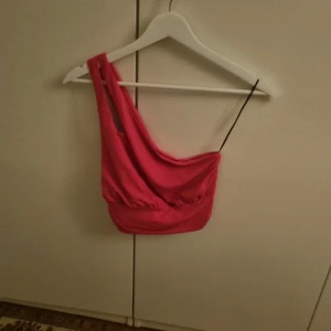 Rosa one shoulder topp från H&M - Säljer en rosa one shoulder topp från H&M i storlek S. Toppen är croppad med en axelbandslös design på ena sidan och ett smalt band på andra. Tillverkad i mjuk bomullsmix, perfekt för en trendig look.