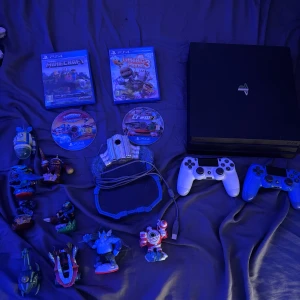 PlayStation 4 Pro + 2 kontroller + spel och Skylanders-figurer - PlayStation 4 Pro i bra skick med två DualShock 4-kontroller (vit och blå). Inkluderar spelen Minecraft, LittleBigPlanet 3, The Crew 2 och Skylanders SuperChargers samt flera Skylanders-figurer och portal. Perfekt paket för familjen eller samlaren!