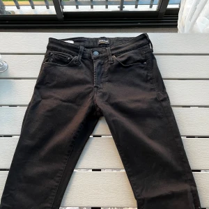 Svarta jeans från Jack & Jones - Svarta jeans från Jack & Jones med klassisk femficksdesign och diskret logga på bakfickan. Jeansen har en rak passform och är tillverkade i ett mjukt bomullsmaterial med lite stretch för extra komfort. Perfekta för en clean och stilren look.