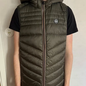 Dunväst från Jack & Jones - Aldrig använd Olivgrön dunväst från Jack & Jones med huva och dragkedja framtill. (Katt finns i hemmet) nypris 300kr (dragkedjan är lite trög då den aldrig är använd) storlek 176