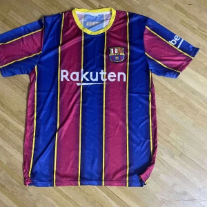 FC Barcelona Messi 10 matchtröja - Säljer en officiell FC Barcelona fotbollströja med Messi 10 på ryggen. Tröjan har klassiska blå och röda vertikala ränder med gula detaljer, klubbmärke på bröstet och Rakuten som sponsor. Kortärmad modell i lätt och ventilerande material.