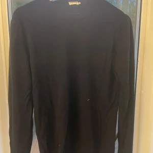 Svart långärmad stickad tröja - En stilren svart stickad tröja från Filippa K med rund halsringning och långa ärmar. Perfekt för dig som gillar en enkel och klassisk look. Tröjan är mjuk och passar till många olika outfits.