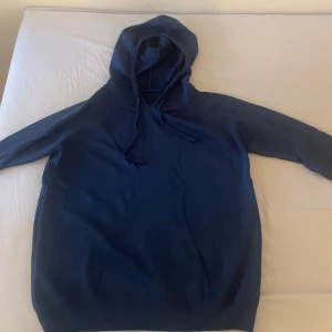 Mörkblå hoodie med huva (cashmere) och snörning - En stilren mörkblå hoodie med huva (cashmere) och snörning. Tröjan har långa ärmar och är tillverkad i ett mjukt material som känns skönt mot huden. Perfekt för dig som gillar en enkel och klassisk look.