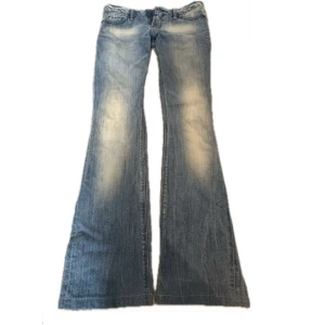 Blå bootcut jeans med detaljer - Snygga blå bootcut jeans med slitningar och ljusa partier framtill. Baktill finns två fickor med dekorativa sömmar och små nitar. Jeansen har klassisk femficksdesign och låg midja, perfekta för dig som gillar retrovibbar och coola detaljer.