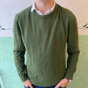 Olivgrön tröja från Riley - Säljer en stilren olivgrön tröja från Riley i storlek S. Tröjan har rund halsringning, långa ärmar och är tillverkad i ett mjukt, stickat material som känns skönt mot huden. Perfekt att bära över en skjorta för en clean look.