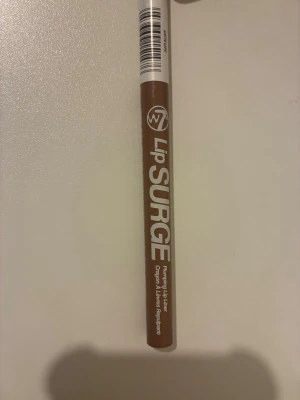 W7 Lip Surge läppenna brun - Testat två gånger. Säljer en W7 Lip Surge plumping läppenna i en snygg brun nyans. Pennan har en klassisk smal form som gör det enkelt att markera och forma läpparna. Perfekt för att skapa fylligare läppar och definierade konturer.