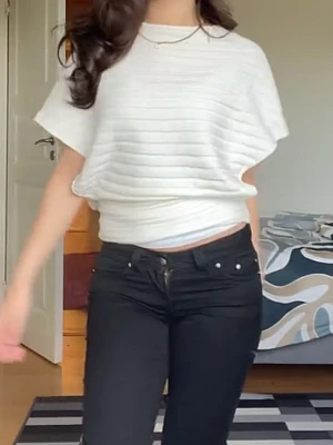 Vit ribbad topp med kort ärm - Säljer en vit topp med diskreta horisontella ribbade ränder. Toppen har korta, lösa ärmar och en avslappnad passform som sitter snyggt i midjan. Perfekt till jeans eller kjol för en clean look.