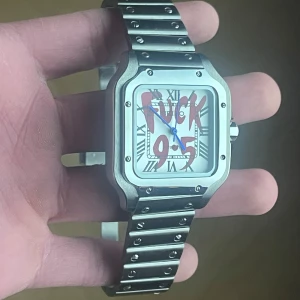 Seiko Mod Santos “F*ck 9–5” – Silver - ✨ Specifikationer Modell: Seiko Mod Santos ⌚ Urverk: Automatiskt Seiko-urverk Gångreserv: 41 timmar ⏳ Boett: Rostfritt stål med borstade och polerade ytor Storlek: 40 mm 📏 Glas: Reptåligt safirglas 💎 Urtavla: Vit tavla med romerska siffror och röd “F*ck 9–5”-text 🔥