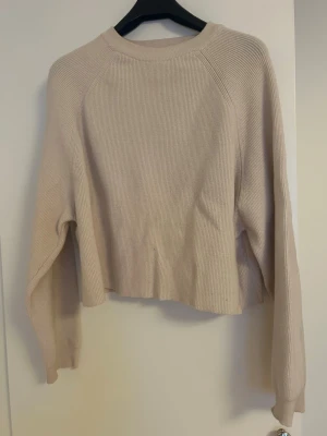 Beige stickad tröja med lång ärm - Säljer en beige stickad tröja med ribbad struktur och rund hals. Tröjan har lång ärm och en något croppad passform som ger en avslappnad vibe. Perfekt att matcha med jeans eller kjol för en enkel och snygg look.