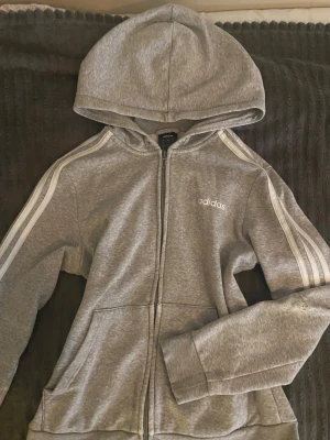 Grå Adidas tröja - Säljer denna fina gråa adidas tröja i storlek M. Passar S också! Den är använd men är fortfarande i bra skick, men har ett litet hål i armbågen som antagligen går att laga.