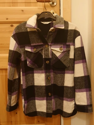 Rutig overshirt från H&M - Säljer en snygg rutig kappa från H&M i svart, vit, grå och lila. Jackan har stora knappar framtill, två bröstfickor med lock och den har mjukt material.☺️💕