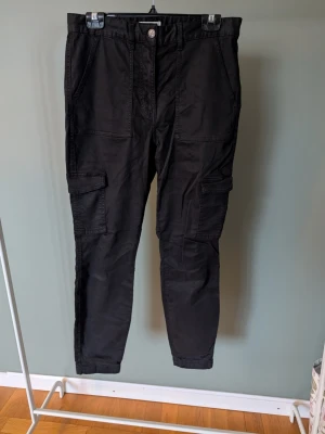 Svarta cargobyxor från H&M - Svarta cargobyxor från H&M med flera praktiska fickor på benen och normal passform. Tillverkade i bomull med en knapp och dragkedja i midjan. Perfekta för en avslappnad och cool stil.