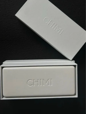 Beige solglasögon från CHIMI - Snygga solglasögon från CHIMI med transparent beige båge och bruna linser. Glasögonen har en fyrkantig form och kommer med ett vitt fodral och tygpåse. Perfekt accessoar för soliga dagar och ger en cool vibe till din outfit.