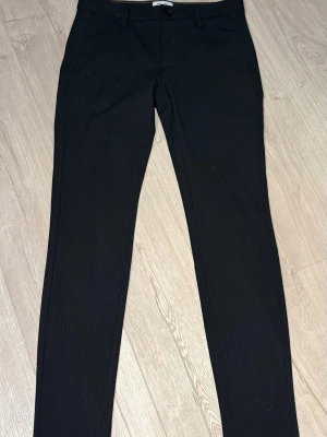 Svarta kostymbyxor med diskret rand - Svarta kostymbyxor med en svaga lodräta linjer i vitt från Only&sons. Dom är i stretchigt material. Midjemått är 30 och längdmått 34.