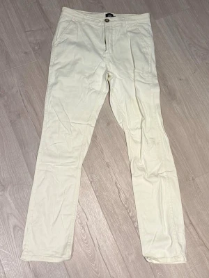Vita chinos med normal passform - Snygga vita chinos med raka ben och klassisk knappgylf. Byxorna har sidofickor och hällor för bälte, perfekta för en clean och stilren look. Tillverkade i mjukt bomullstyg som känns bekvämt hela dagen. Storlek M, Storlek Vit/beige ish