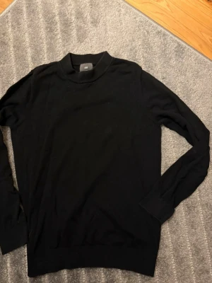 Svart sweatshirt med krage  - Säljer en svart sweatshirt med krage från H&M med enkel och stilren design i storlek S. Tröjan har lång ärm och en hög krage som ger en snygg look. Perfekt att matcha med jeans för en clean outfit. Materialet är mjukt och skönt, troligtvis bomull eller polyester. 