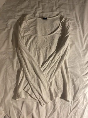 Vit långärmad topp med rund hals - Säljer en enkel och stilren vit långärmad topp med rundad halsringning. Toppen är i mjukt och tunt material, perfekt för layering eller att bära som den är. Passar dig som gillar minimalistisk stil och neutrala färger.