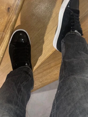 Lanvins  - Säljer ett par svarta sneakers med vit sula och snörning. Skorna har en blank tådel och resten av skon är i mockaliknande material. Klassisk och stilren design som passar till det mesta.