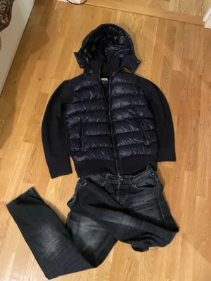 Mörkblå pufferjacka från Cevior - Säljer en mörkblå pufferjacka från Cevior i storlek S. Jackan har quiltad kropp, stickade ärmar och huva. Dragkedja framtill och två fickor med dragkedja. Perfekt för kyliga dagar och riktigt snygg till jeans.