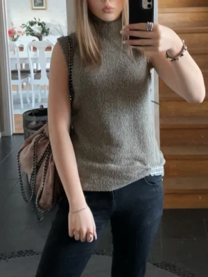 Grön ribbad polotopp ärmlös - Säljer en stilren grön polotopp i ribbat material. Toppen är ärmlös och har en hög krage som ger en clean look. Perfekt att matcha med både jeans och kjol för en trendig outfit.