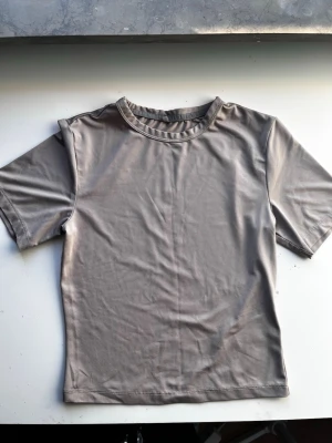 Grå kortärmad t-shirt från H&M Move - Säljer en stilren grå t-shirt från H&M Move i storlek S. T-shirten har korta ärmar, rund halsringning och är gjord i ett mjukt, stretchigt syntetmaterial som passar perfekt till träning. Diskret Move-logga i nacken.